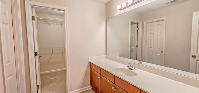 bathroom with visible vents, vanity, baseboards, and a spacious closet