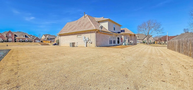 back of house featuring cooling unit, brick siding, a residential view, and fence