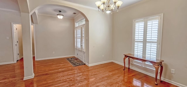 foyer entrance featuring arched walkways, a chandelier, wood finished floors, baseboards, and crown molding