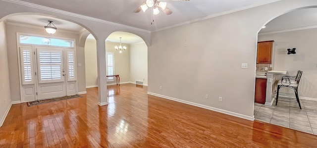 foyer entrance featuring visible vents, arched walkways, baseboards, light wood-style flooring, and ornamental molding