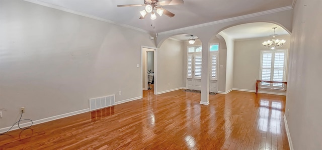 empty room featuring arched walkways, visible vents, light wood-style flooring, ornamental molding, and baseboards