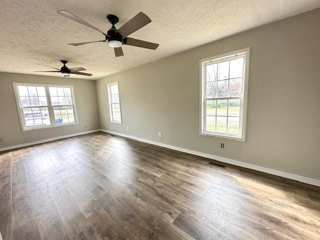 empty room featuring dark wood-style floors, visible vents, a textured ceiling, and baseboards