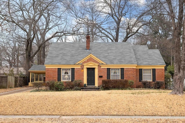 cape cod house with brick siding, a chimney, fence, a carport, and a front lawn