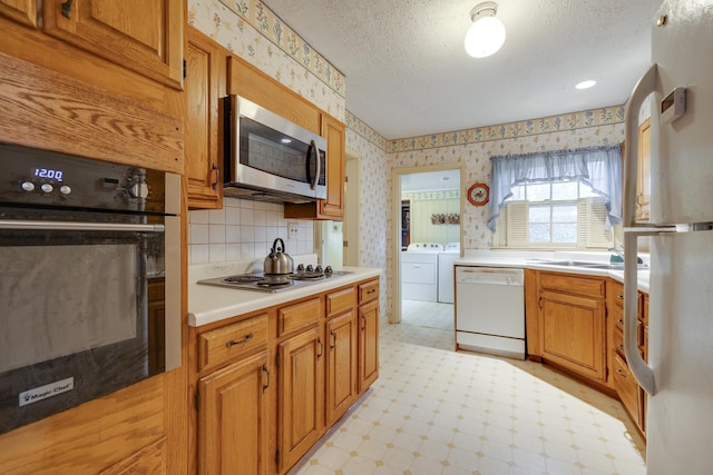 kitchen with wallpapered walls, stainless steel appliances, a textured ceiling, washer and dryer, and light floors