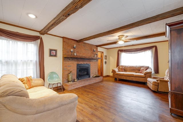 living area with ornamental molding, a brick fireplace, wood finished floors, beamed ceiling, and baseboards