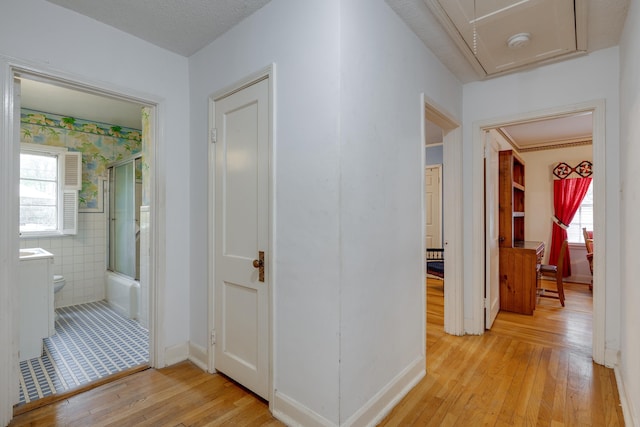 hall featuring attic access, light wood-type flooring, a wealth of natural light, and tile walls