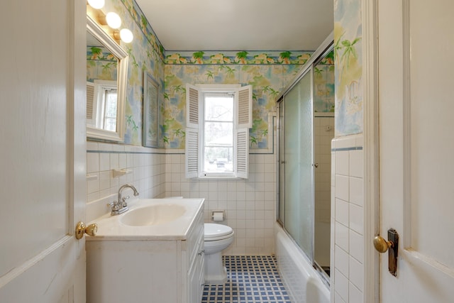 full bath featuring toilet, vanity, tile walls, wainscoting, and wallpapered walls