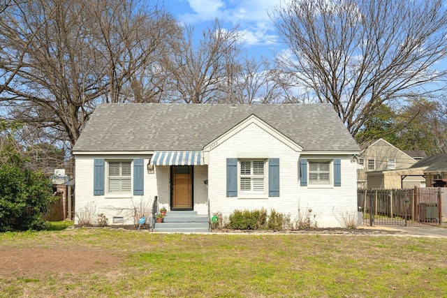 bungalow featuring roof with shingles, brick siding, a front lawn, and fence