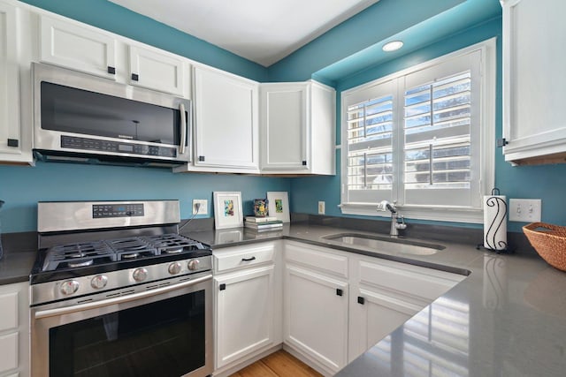 kitchen featuring appliances with stainless steel finishes, dark countertops, white cabinets, and a sink