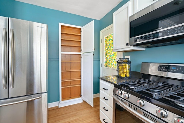 kitchen with baseboards, light wood-style floors, white cabinets, appliances with stainless steel finishes, and dark countertops