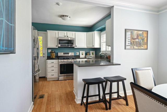 kitchen featuring a breakfast bar area, stainless steel appliances, a peninsula, visible vents, and white cabinetry