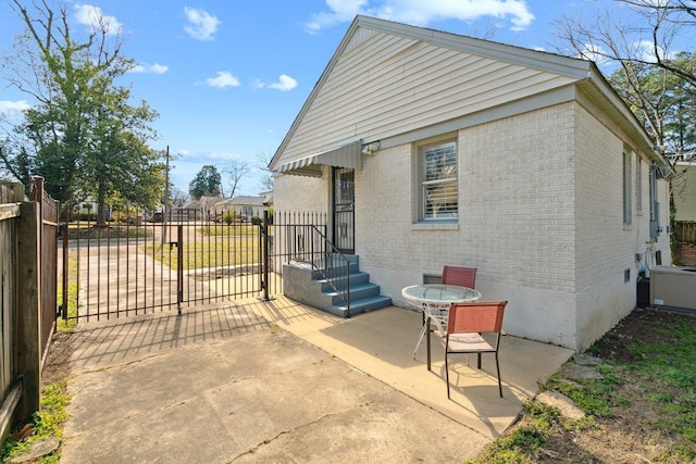 view of property exterior featuring a patio area, brick siding, fence, and outdoor dining area