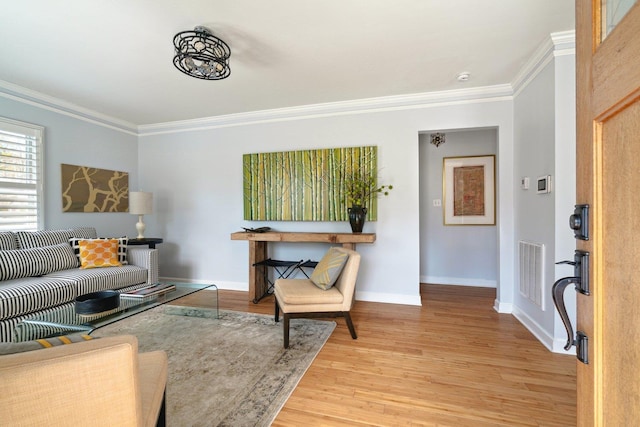 living room featuring ornamental molding, light wood-type flooring, visible vents, and baseboards