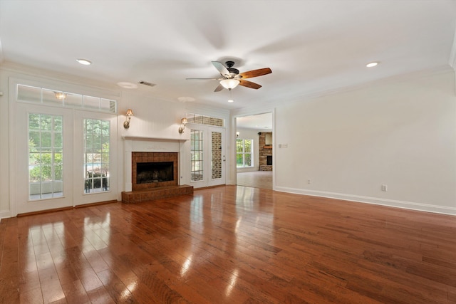 unfurnished living room with hardwood / wood-style flooring, visible vents, a fireplace with raised hearth, and crown molding