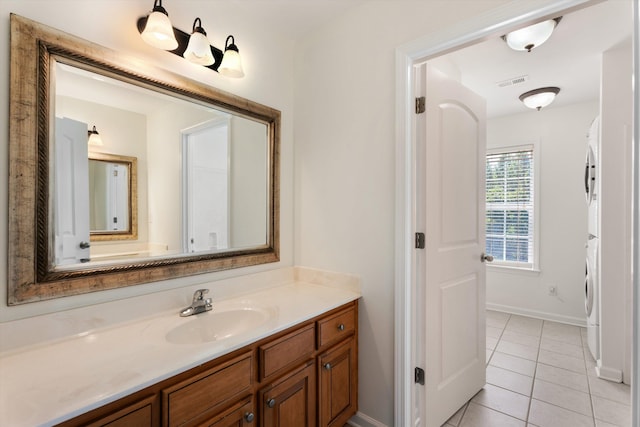 bathroom featuring stacked washer and dryer, baseboards, visible vents, tile patterned floors, and vanity