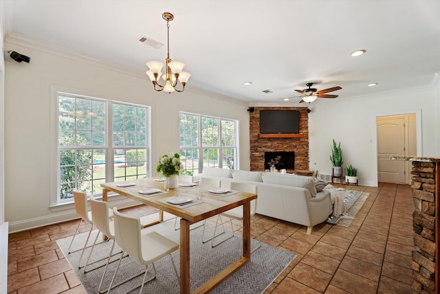 dining space featuring visible vents, crown molding, a stone fireplace, and baseboards