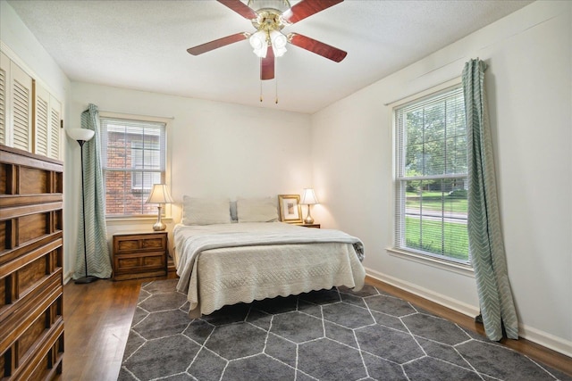 bedroom with a ceiling fan, a textured ceiling, baseboards, and dark wood-style flooring