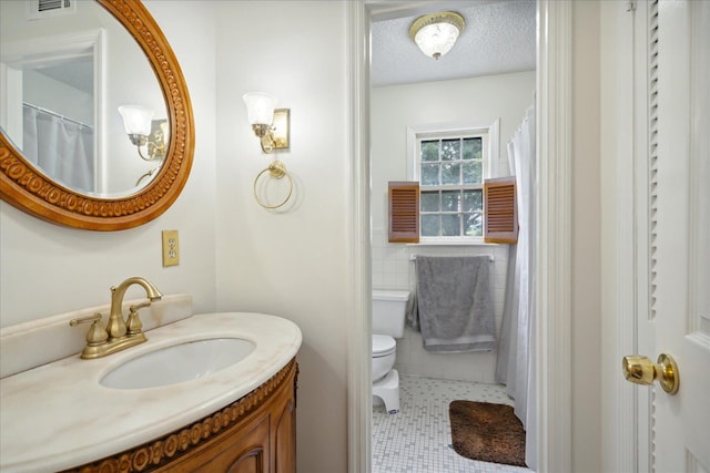 bathroom with a textured ceiling, toilet, tile walls, vanity, and tile patterned floors
