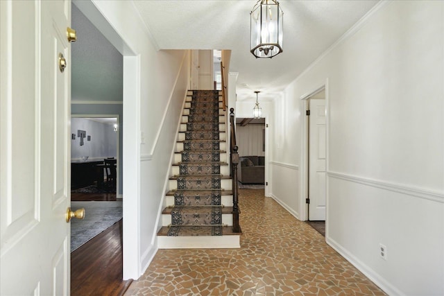 entryway with an inviting chandelier, ornamental molding, a textured ceiling, baseboards, and stairs
