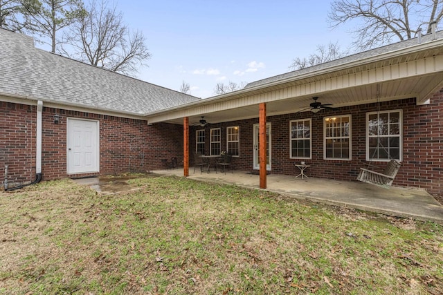 back of property with a patio, brick siding, a shingled roof, a ceiling fan, and a lawn