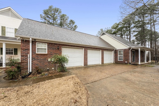 view of side of property with a garage, brick siding, a shingled roof, and driveway