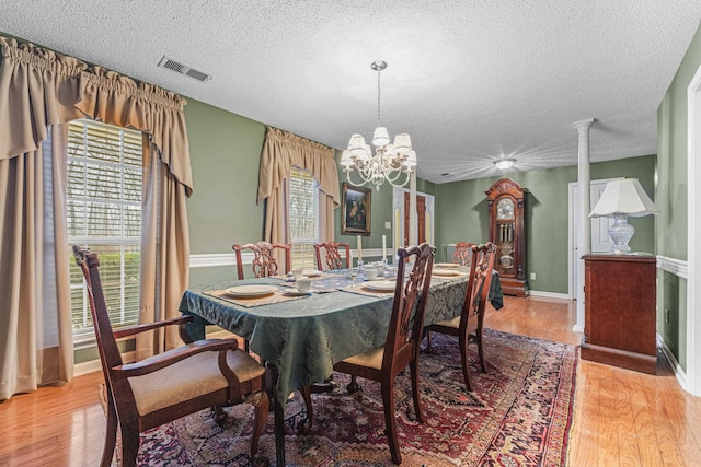 dining space with a textured ceiling, visible vents, baseboards, light wood-style floors, and an inviting chandelier