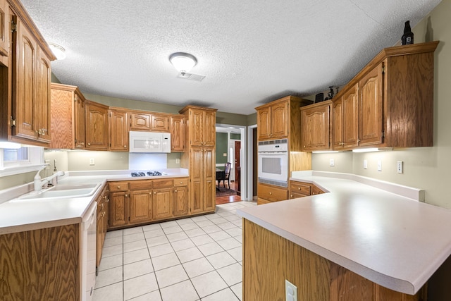 kitchen with brown cabinets, visible vents, light tile patterned flooring, a sink, and white appliances