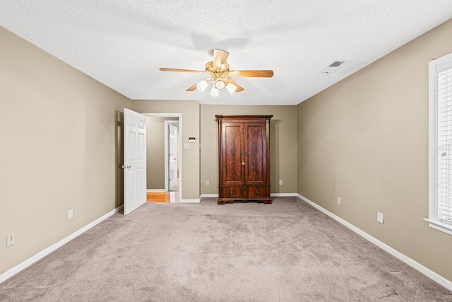 unfurnished bedroom with a textured ceiling, a ceiling fan, light colored carpet, and baseboards