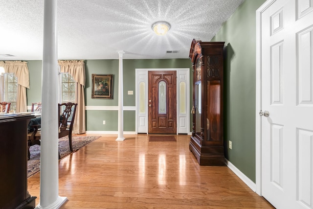 foyer entrance featuring decorative columns, light wood finished floors, visible vents, a textured ceiling, and baseboards