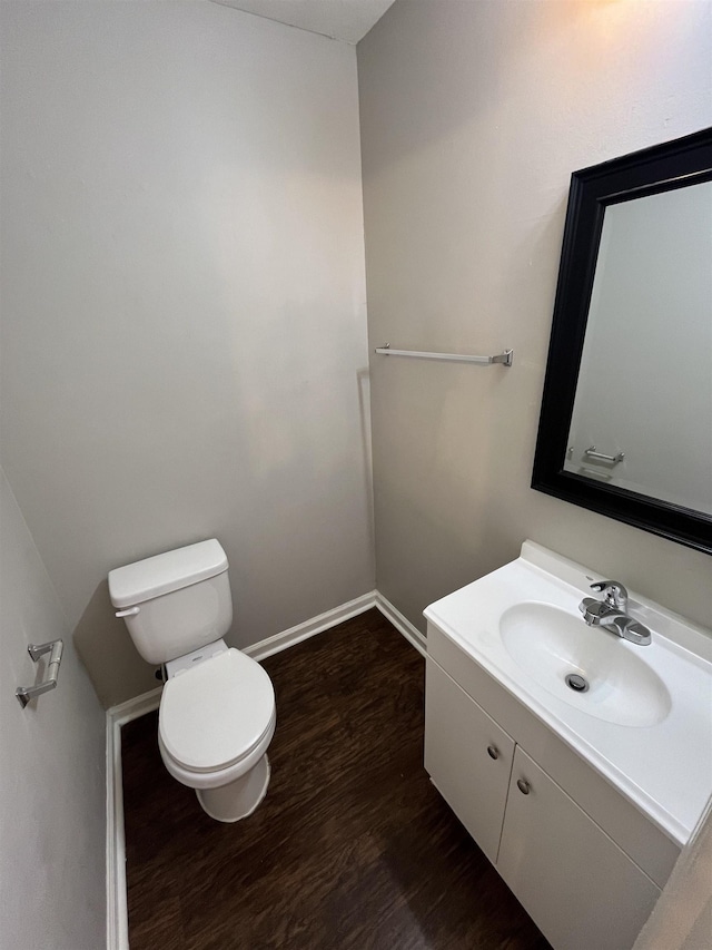 half bath with baseboards, vanity, toilet, and wood finished floors