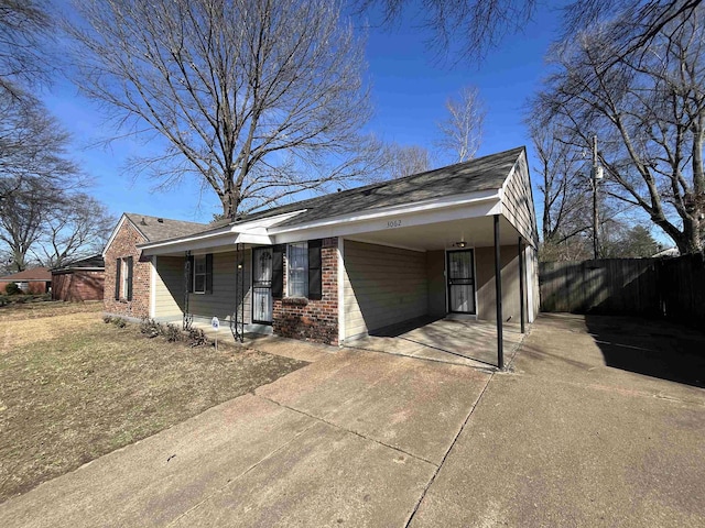 view of front facade featuring an attached carport, concrete driveway, brick siding, and fence