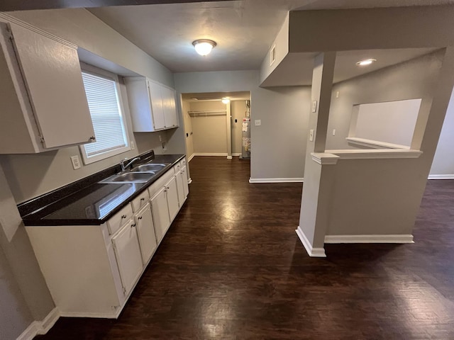 kitchen with a sink, baseboards, white cabinets, dark countertops, and dark wood finished floors