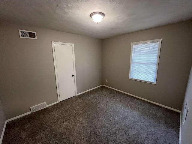 empty room with baseboards, visible vents, and dark carpet