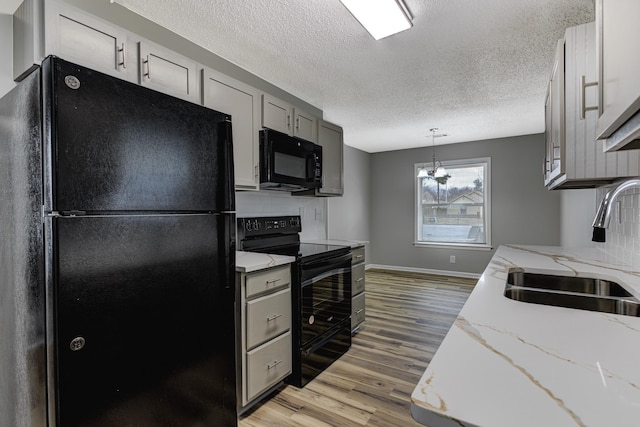 kitchen with gray cabinetry, decorative backsplash, light wood-style floors, a sink, and black appliances