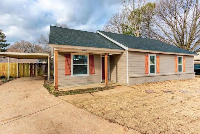 view of front of house featuring roof with shingles, brick siding, concrete driveway, fence, and a carport