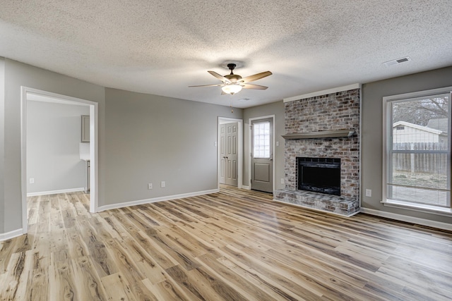 unfurnished living room featuring ceiling fan, a fireplace, visible vents, and light wood-style floors