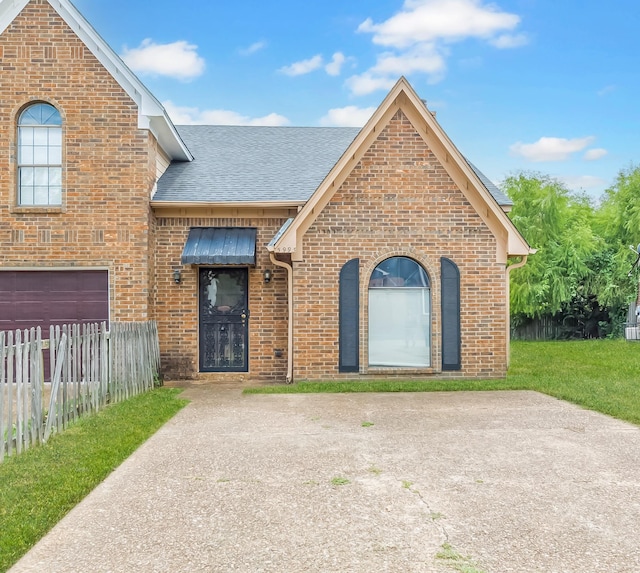 view of front facade with brick siding, a shingled roof, fence, driveway, and a front lawn