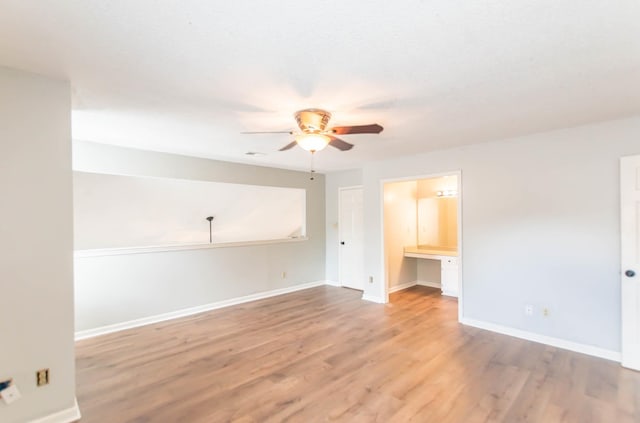 empty room featuring light wood-style flooring, ceiling fan, built in desk, and baseboards