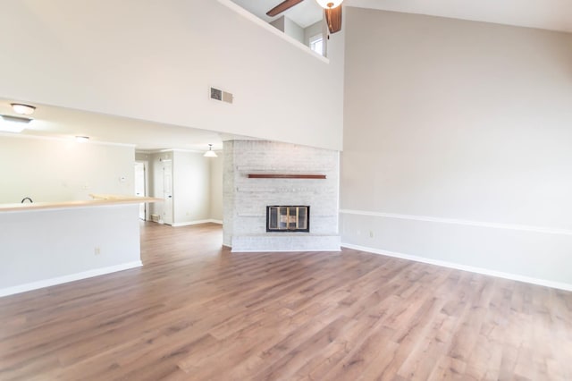 unfurnished living room featuring a fireplace, wood finished floors, visible vents, baseboards, and a ceiling fan