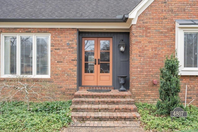 view of exterior entry with roof with shingles, french doors, and brick siding