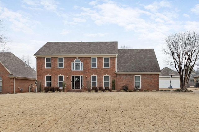 colonial inspired home featuring brick siding and a shingled roof