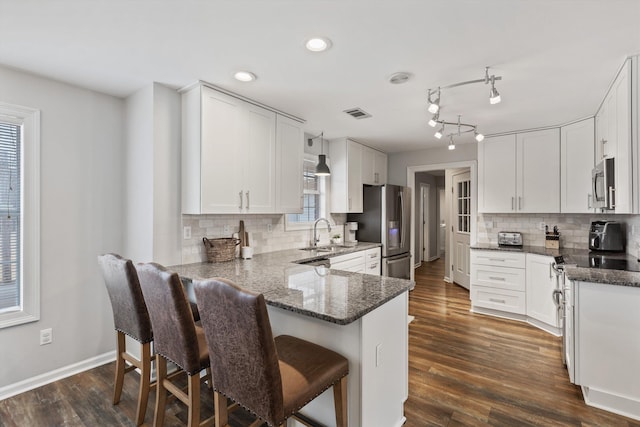 kitchen with dark stone countertops, stainless steel appliances, a peninsula, and a sink