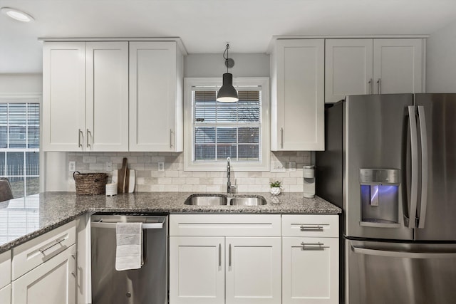 kitchen with tasteful backsplash, white cabinets, dark stone countertops, stainless steel appliances, and a sink