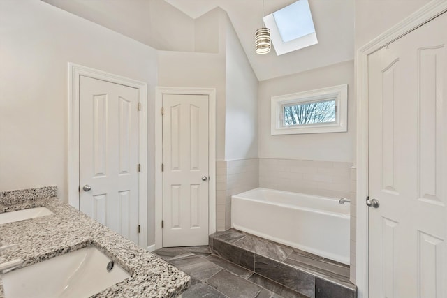 bathroom featuring vaulted ceiling with skylight, double vanity, a sink, and a bath