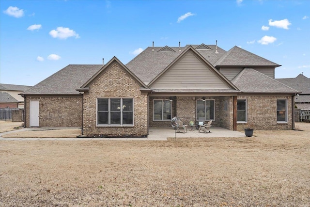 rear view of house with a shingled roof, brick siding, a patio, and a lawn