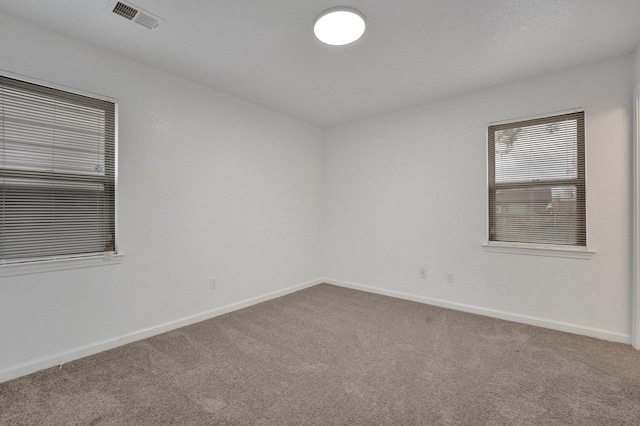 empty room with carpet flooring, visible vents, and baseboards