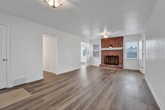 unfurnished living room with a healthy amount of sunlight, a fireplace, visible vents, and dark wood-style flooring