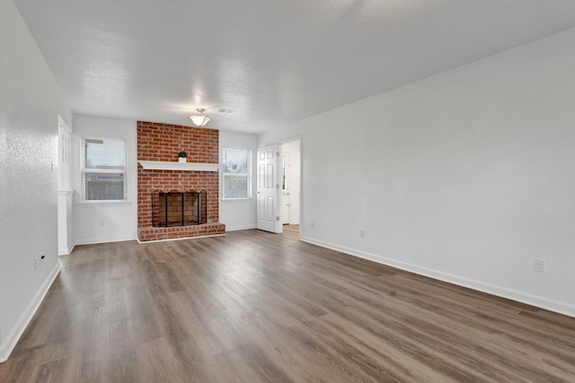 unfurnished living room featuring a brick fireplace, baseboards, dark wood-style floors, and a textured ceiling