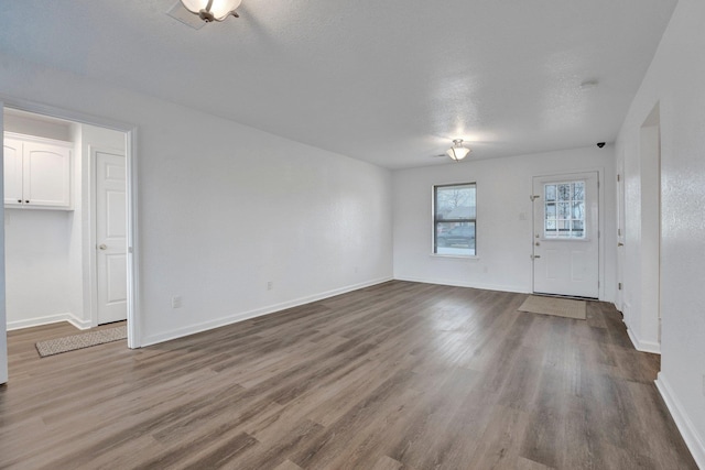 unfurnished living room with dark wood-type flooring, a textured ceiling, and baseboards