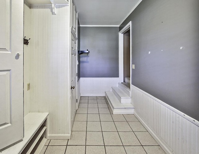 corridor featuring light tile patterned floors, ornamental molding, and wainscoting